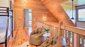 Ein gemütliches Blockhaus mit Holzvertäfelung, einem Etagenbett, zwei Sitzsäcken, einem kleinen Tisch mit einer Pflanze und Blick durch ein Fenster.
