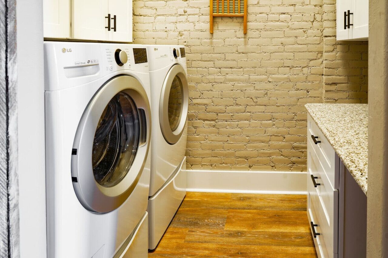 A laundry room with two white LG Direct Drive washing machines, a wooden floor, and a brick wall.