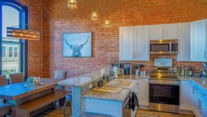 A kitchen with a brick wall, white cabinets, a stainless steel oven, and a sign that reads "FARM FRESH". - West Empire Theatre Loft, Gorgeous Space on Main Street for 4! Local Golfing 50% Off! (Baker City)
