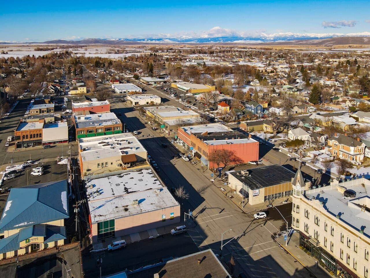 An aerial view of a town with a mix of commercial and residential buildings, including a prominent red building and a large blue-roofed structure.