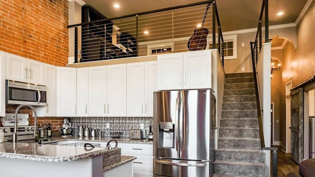 A modern kitchen with white cabinets, a stainless steel refrigerator, and a brick wall. - West Empire Theatre Loft, Gorgeous Space on Main Street for 4! Local Golfing 50% Off! (Baker City)