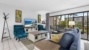 Un salon moderne doté d’un grand téléviseur, de fauteuils turquoise, d’un canapé et d’un coin repas offrant une vue sur l’océan.
