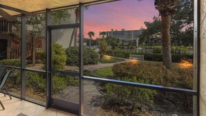 Une chambre d’hôtel moderne dotée de grandes portes vitrées donnant sur un jardin avec des palmiers et offrant une vue sur un bâtiment en arrière-plan.