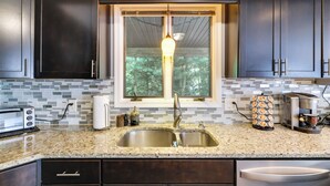 A kitchen with dark cabinets, a granite countertop, a double sink, a window with a view of trees, and a hanging light fixture. - Fire Pit! Lake Harmony Home, 3 Mi to Big Boulder (Lake Harmony)