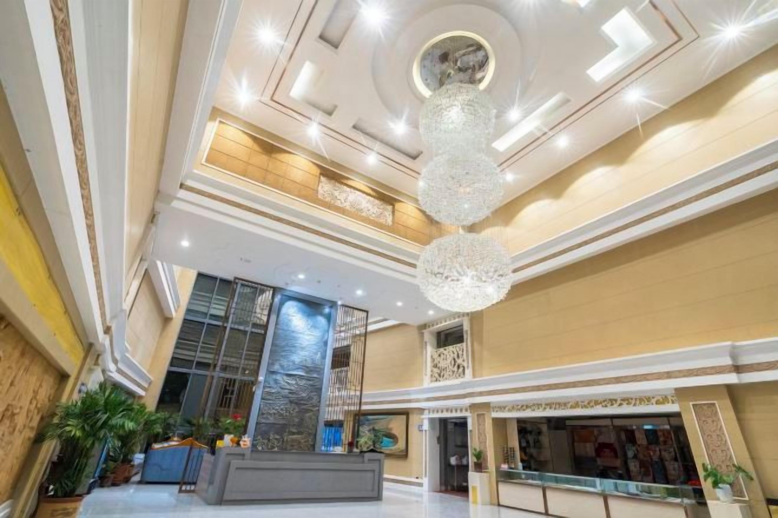 A hotel lobby with a reception desk, a chandelier, and a large window.