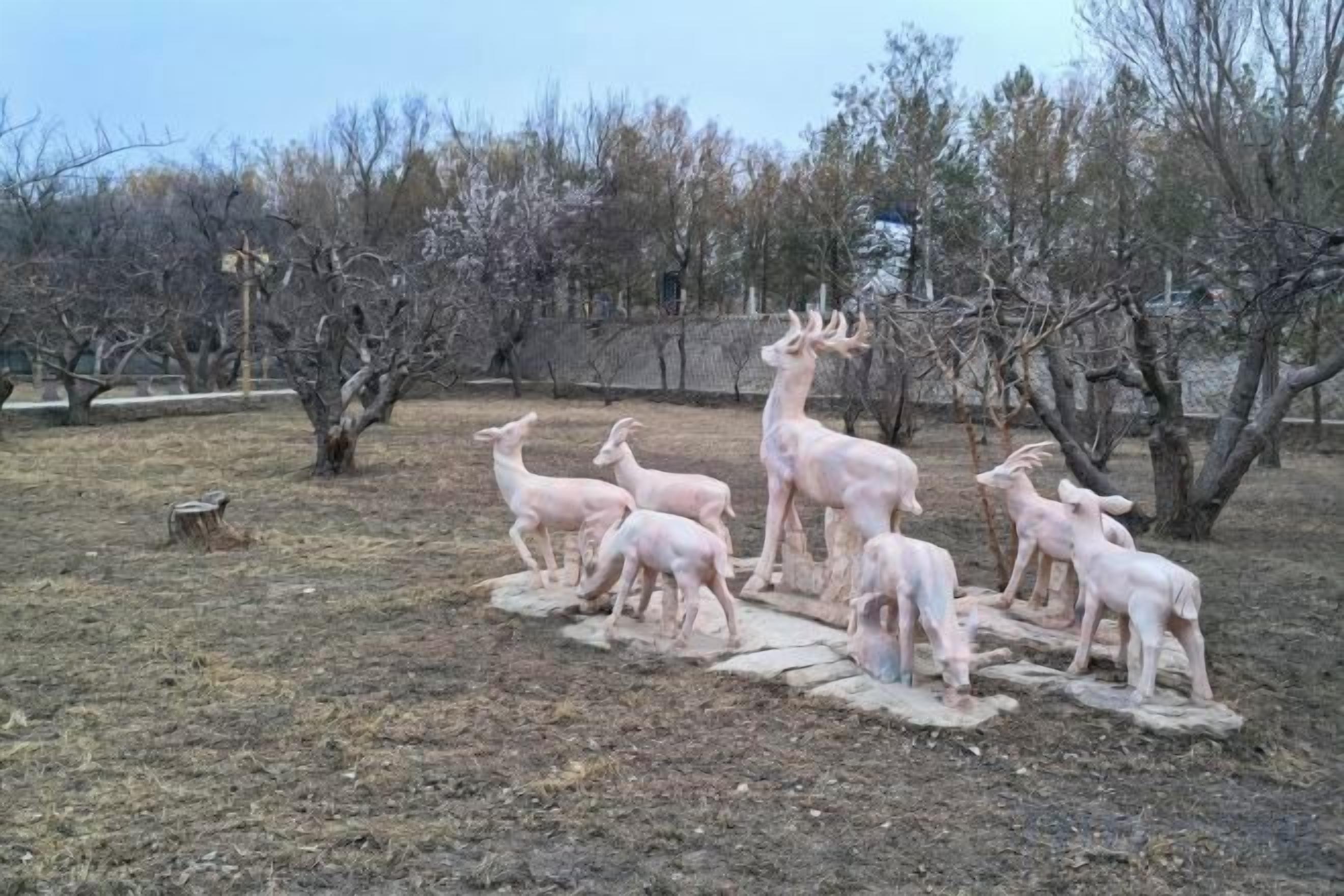 Una escultura de ciervos en un parque, con árboles y una cerca al fondo.