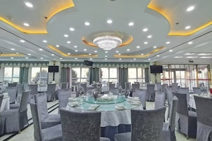 Un salón de conferencias con mesas redondas, sillas, una araña de cristal y ventanas amplias.