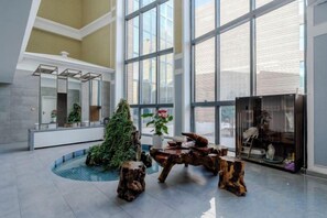 Un hall d’entrée spacieux avec une grande fenêtre, un espace de détente central agrémenté d’une fontaine et un comptoir d’accueil.