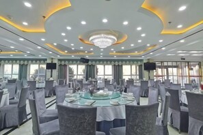 Un salón de conferencias con mesas redondas, sillas, una araña y ventanas amplias.
