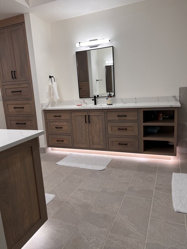 A modern bathroom with a large mirror, wooden cabinets, and a marble countertop.