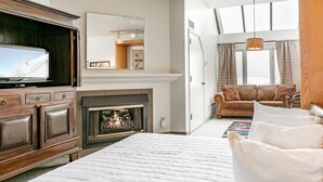Ein Schlafzimmer mit einem großen Bett, einem Kamin, einem Fernseher, einem Sofa und einem Fenster mit Vorhängen.