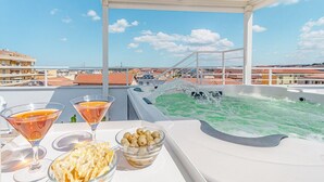 A rooftop terrace with a hot tub, a table with drinks and snacks, and a view of buildings. - Skyfive Fire, Ideal for those who love a carefree holiday. Relaxation and amazement (Alghero)