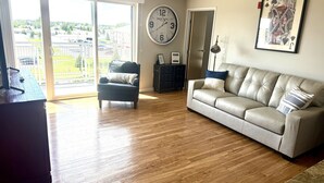 A living room with a sofa, a chair, a clock, and a door leading to a balcony.