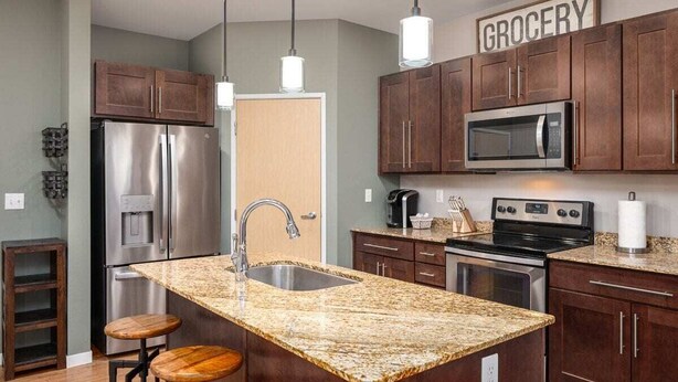 A kitchen with granite countertops, stainless steel appliances, wooden cabinets, and pendant lighting.