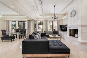 A spacious living room with a black sectional sofa, a fireplace, a television, and a dining area with a glass table and chairs.