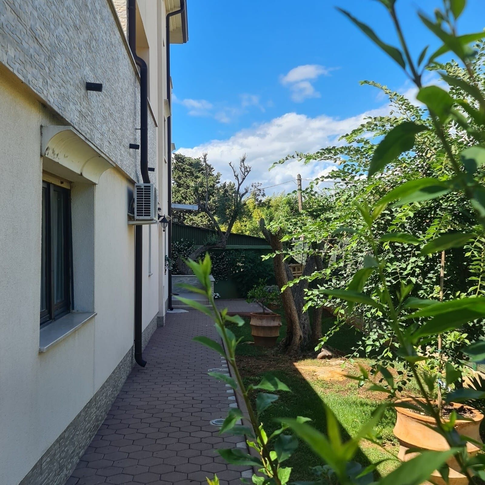 A narrow pathway leading to a building with a window and an air conditioning unit.