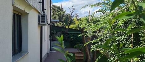 A narrow pathway leading to a building with a window and an air conditioning unit.