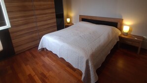 Quarto com uma cama grande, guarda-roupa de madeira e duas luminárias de cabeceira.