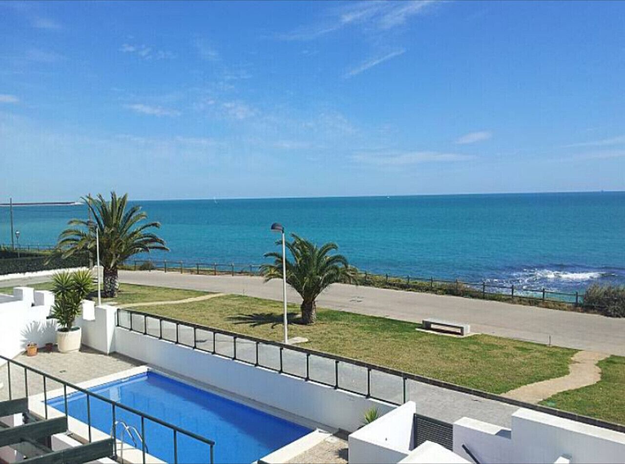 A pool with a view of the sea, a pathway, and some greenery.
