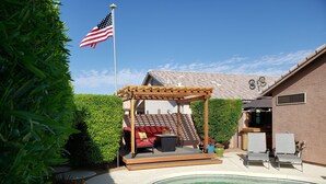 A backyard with a swimming pool, a pergola with outdoor furniture, and a flag. - Beautiful Home with Private Pool and Tiki Bar. Close to Everything!!! (Surprise)