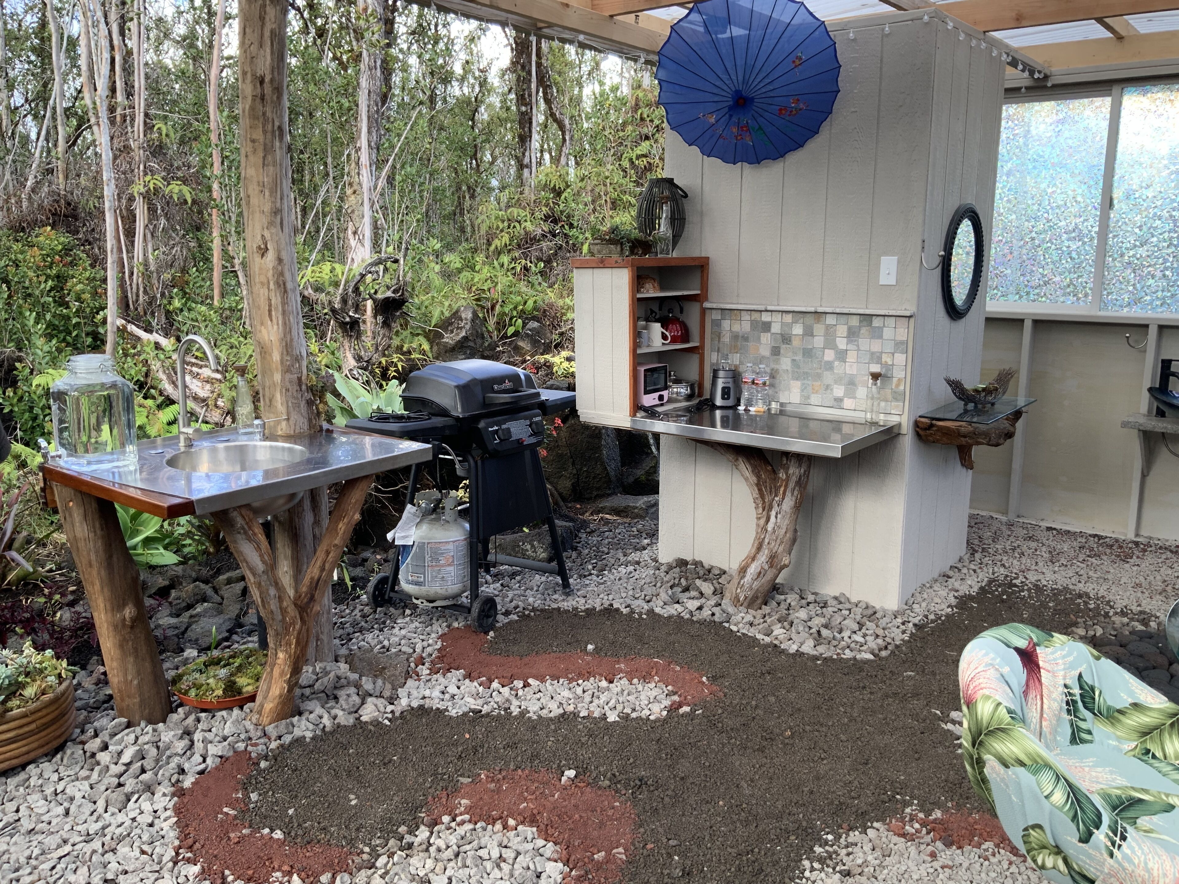 Una cocina rústica al aire libre con una parrilla a gas, un lavamanos y una mesa de madera.