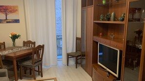 Un salon comprenant une table à manger en bois, des chaises, une table basse en verre, un téléviseur et un meuble avec des portes en verre.