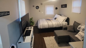 Ein kleines, gut beleuchtetes Schlafzimmer mit einem Bett, einer Couch, einem Fernseher und einem Deckenventilator.