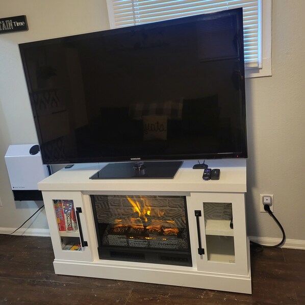 A flat-screen TV on a white entertainment center with a fireplace below.
