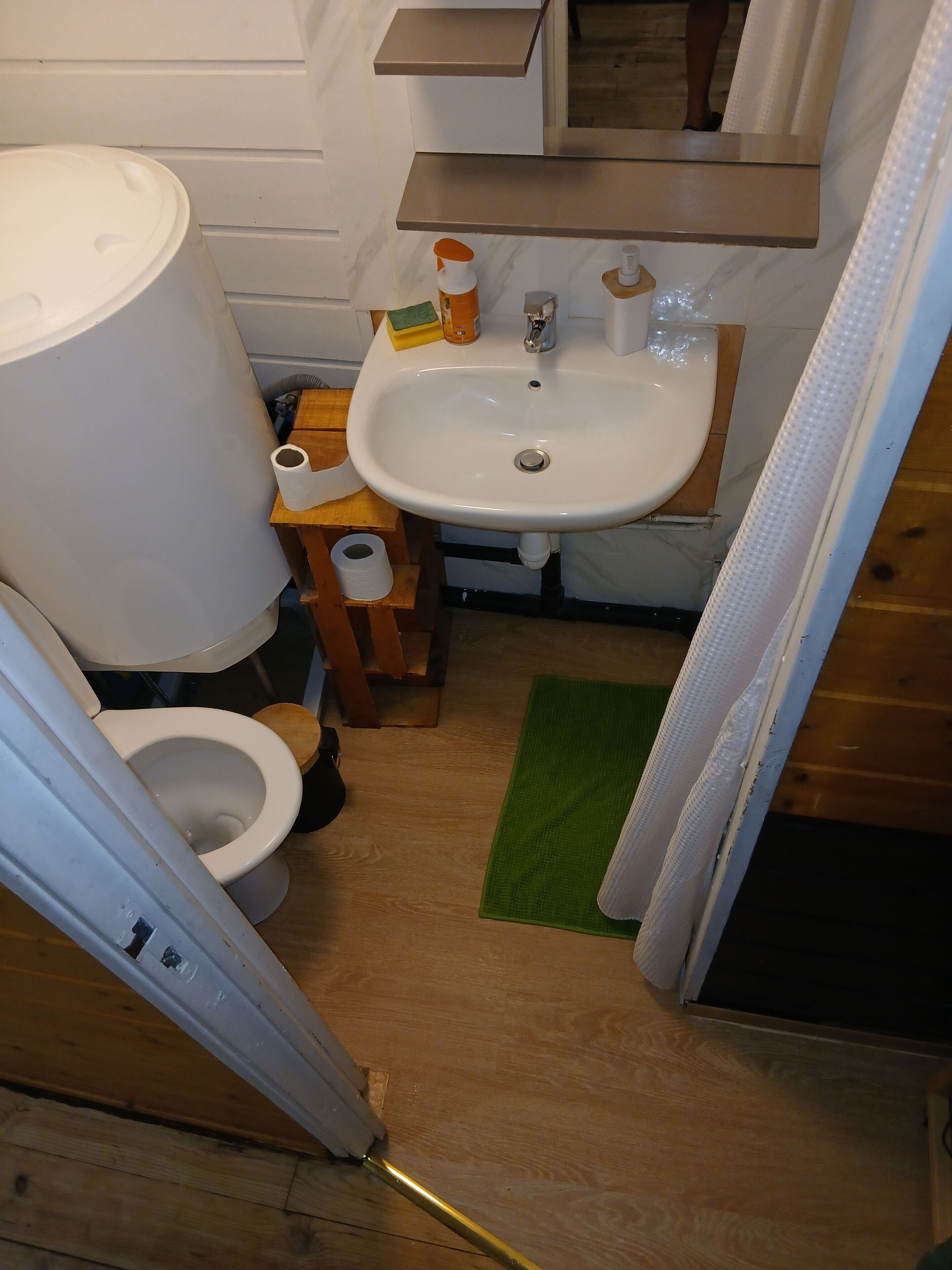 Et badeværelse med toilet, håndvask og en træhylde.