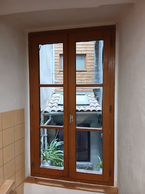Ventana con marco de madera y múltiples vidrios, pared con azulejos y una vista parcial de un tejado con azulejos.
