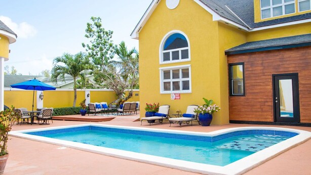 A yellow building with a swimming pool, lounge chairs, and a wooden door. - Sunlite Studio (Nassau)