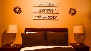 A hotel room with a bed, two bedside tables with lamps, and three wooden signs on the wall. - Sunlite Studio (Nassau)