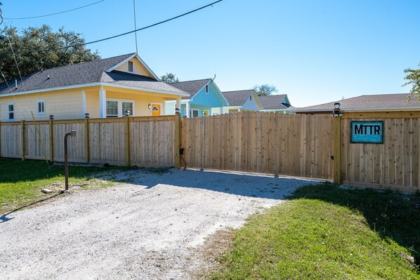 A fenced backyard with a gravel driveway, a wooden fence, and a sign reading "MTTR".