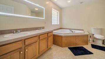 A modern bathroom with two sinks, a bathtub, wooden cabinets, a large mirror, recessed ceiling lights, and a window.