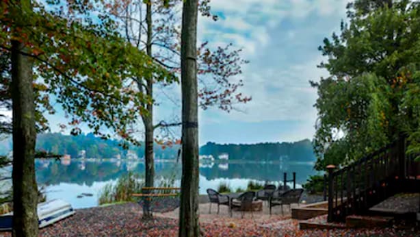 A lakeside seating area with a bench and chairs, surrounded by trees and a view of the lake. - 2900sqft villa near ski & snowboarding (Tobyhanna)