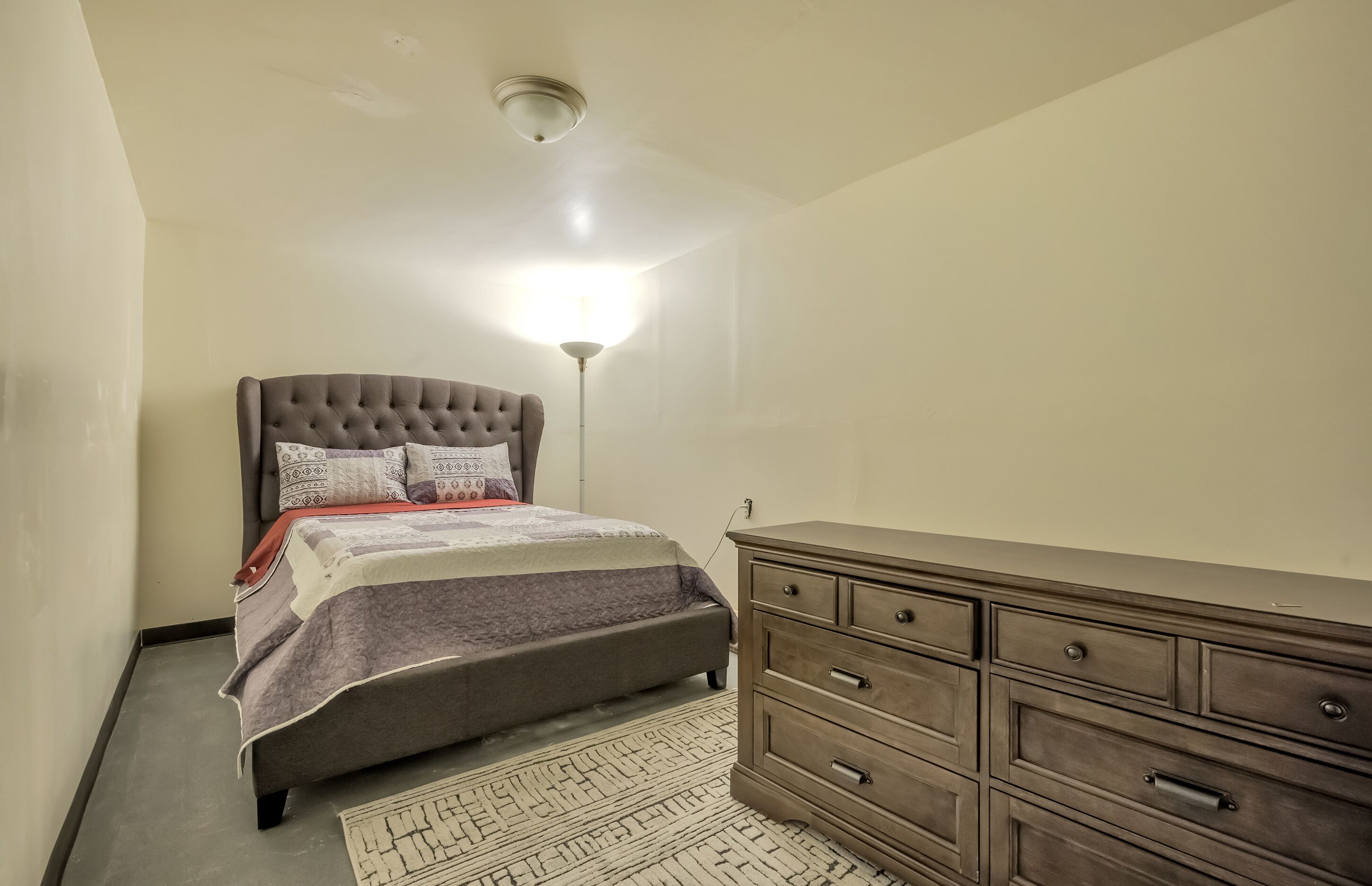 A bedroom with a bed, dresser, and a floor lamp.