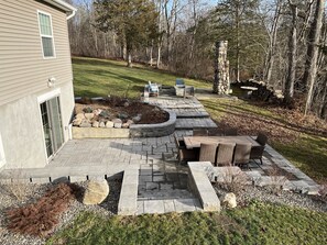 A patio with a stone fire pit, seating area, and a stone column. - Cozy retreat w/ patio & fire pit. Close to Cayuga Lake and Cornell. (Lansing)