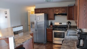 A kitchen with granite countertops, stainless steel appliances, wooden cabinets, and a stainless steel trash can.