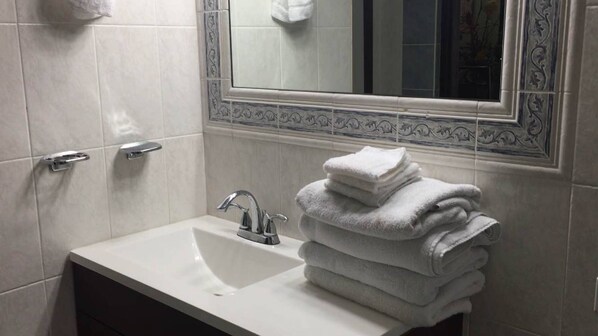 A bathroom with a white sink, a mirror with a decorative frame, and a stack of white towels.