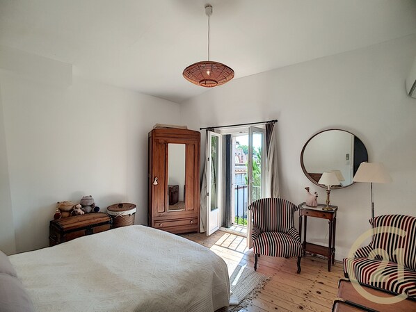 A bedroom with a bed, a wooden wardrobe, a chair, a small table, and a mirror.