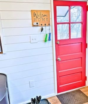 A red door with a window, a welcome sign, and a coat rack with items on it.