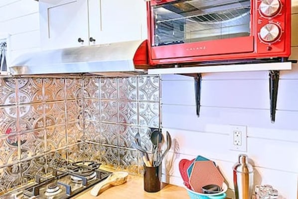 A kitchen with a red toaster oven, a gas stove, and a metal rack with utensils.