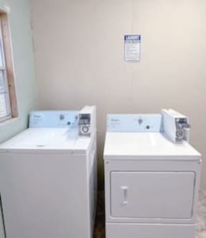 Two white washing machines in a room with a light-colored wall and a window on the left.