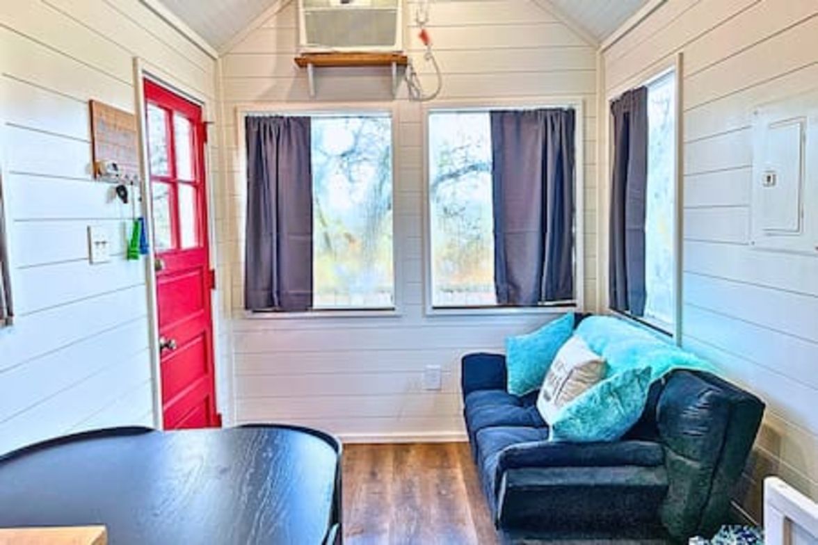 Una habitación acogedora con una mesa negra, una puerta roja y un sofá azul con cojines.