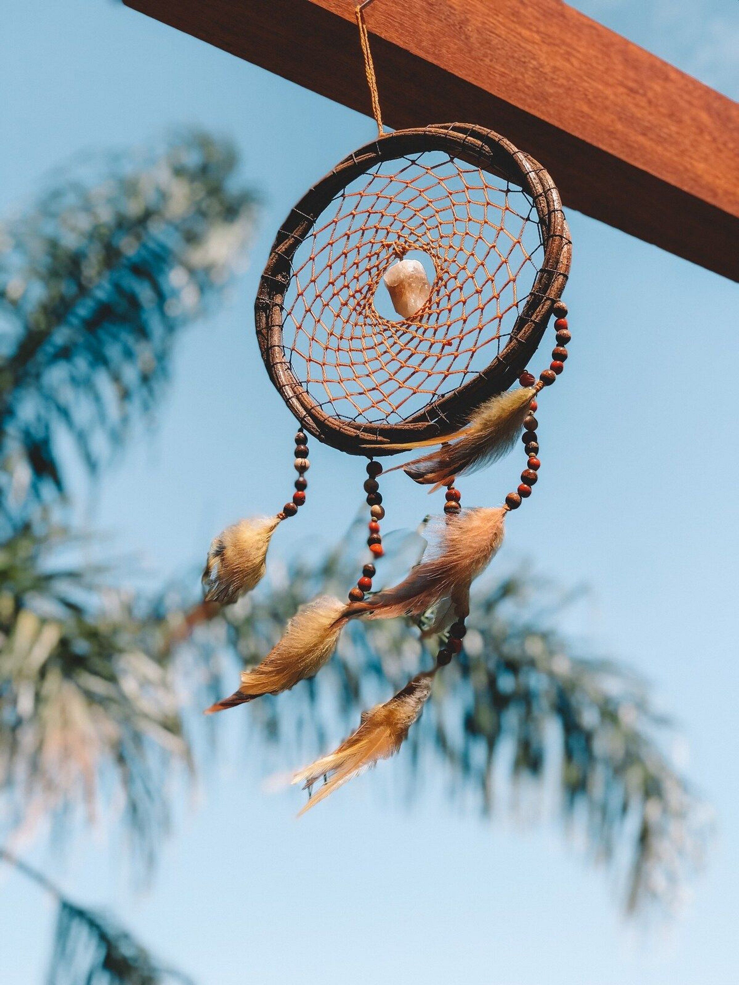 A dreamcatcher with feathers and beads, hanging against a clear sky.