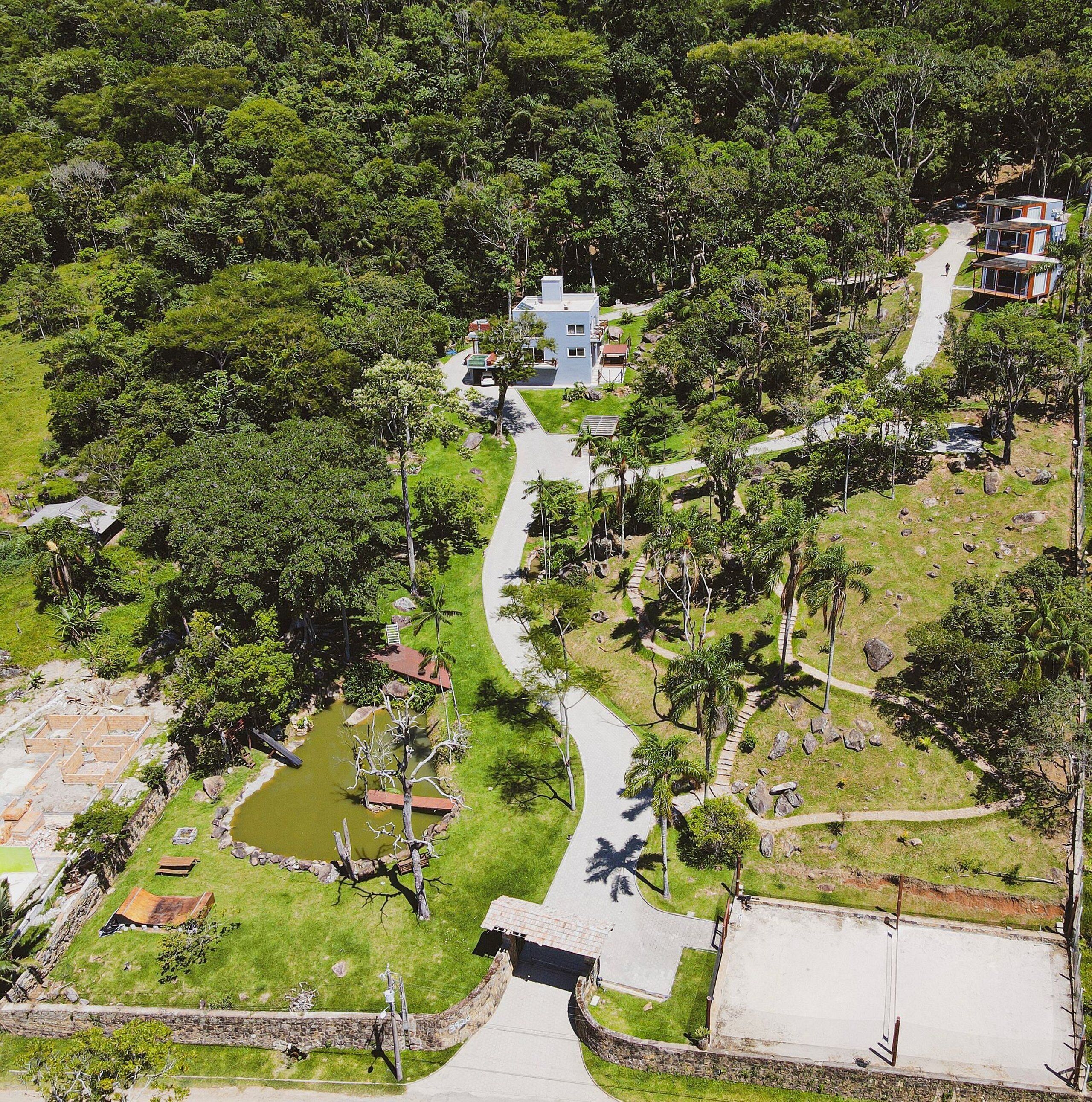 An aerial view of a resort with a central building surrounded by lush greenery, a winding pathway, and a small pond.