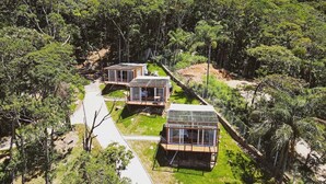 Three modern cabins in a forested area with a paved path leading to them. - Casa de Vidro - Hospedar com Propósito (Florianópolis)