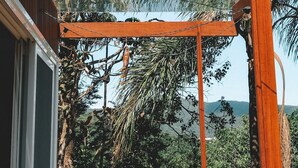 A wooden pergola structure with a view of a tropical landscape, including trees and a distant mountain range. - Casa de Vidro - Hospedar com Propósito (Florianópolis)