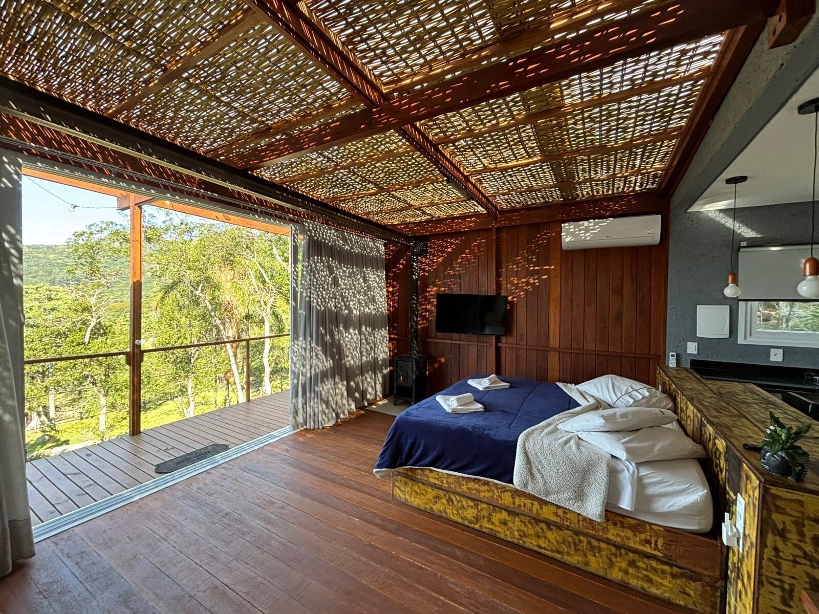 A bedroom with a large bed, a TV, and a wooden ceiling.
