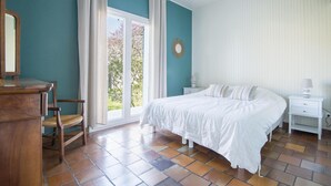A bedroom with a bed, a nightstand, a chair, and a window with curtains. - Villa PIERROT      . (La Flotte)